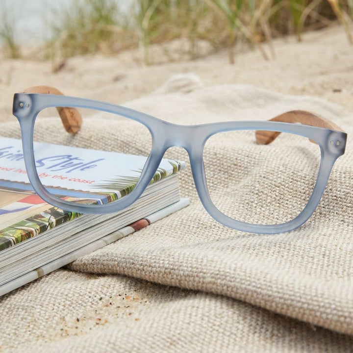 Blue eyeglasses on a magazine with sand and grass in the background